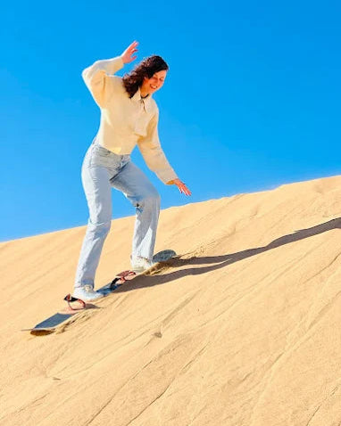 Agadir, Person sandboarding down a sand dune with a clear blue sky.